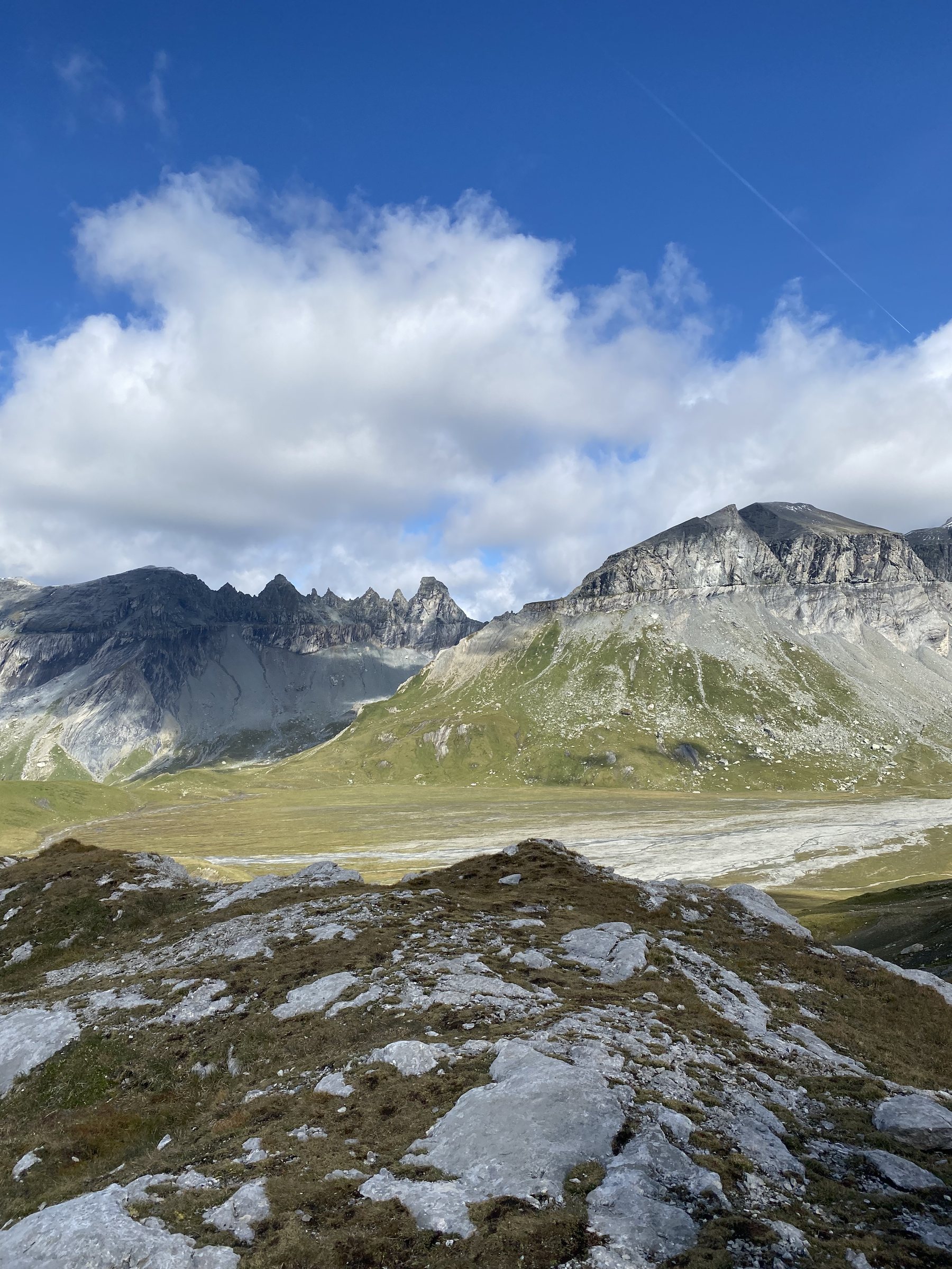 Weites Hochtal mit Schotterebene und Bach, dahinter gezackte Felsgipfel unter blauem Himmel