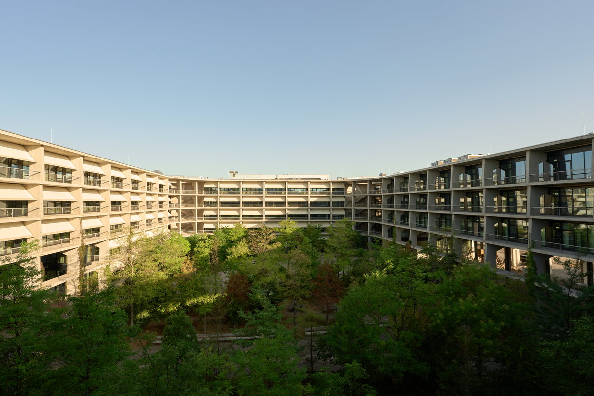 Der geschwungene Bau des SIP Main Campus in Allschwil, im Innenhof dichte Baumgruppen